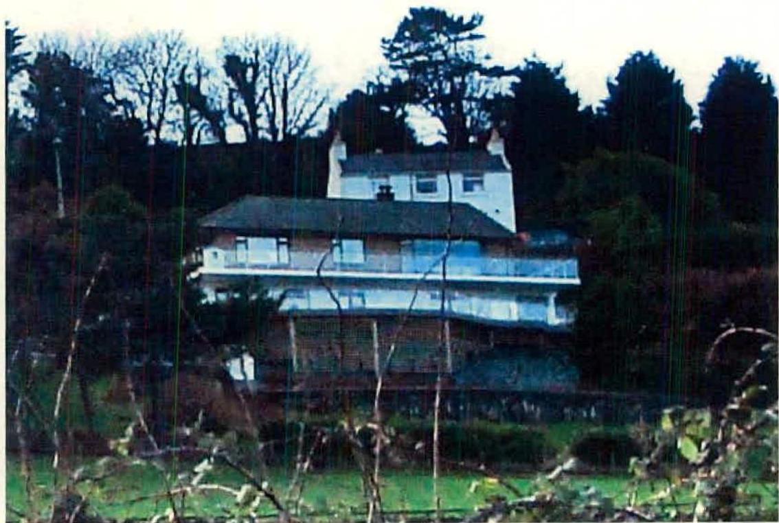 A grainy photograph showing a large white detached house situated on a sloping site with trees in the background.