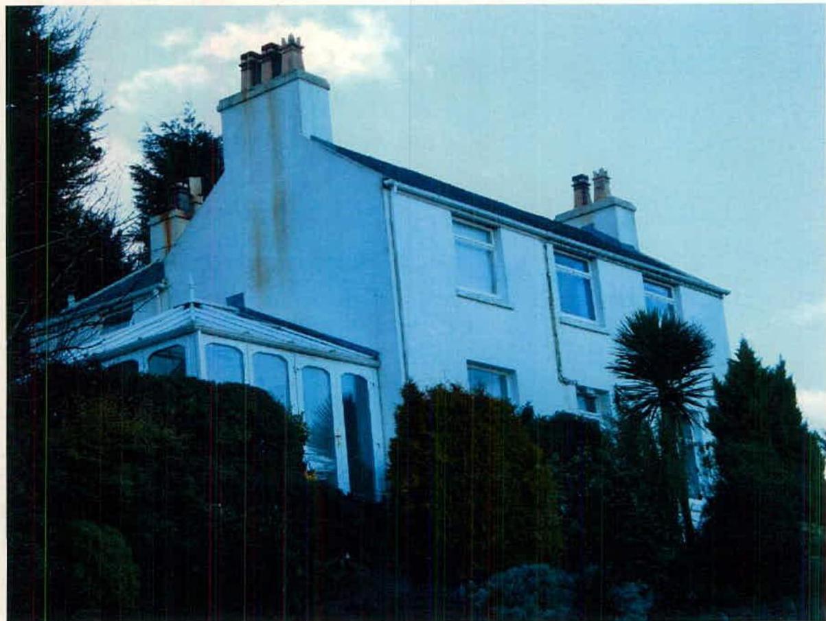 A photograph of a white two-story detached house with a conservatory extension, surrounded by trees and hedges.