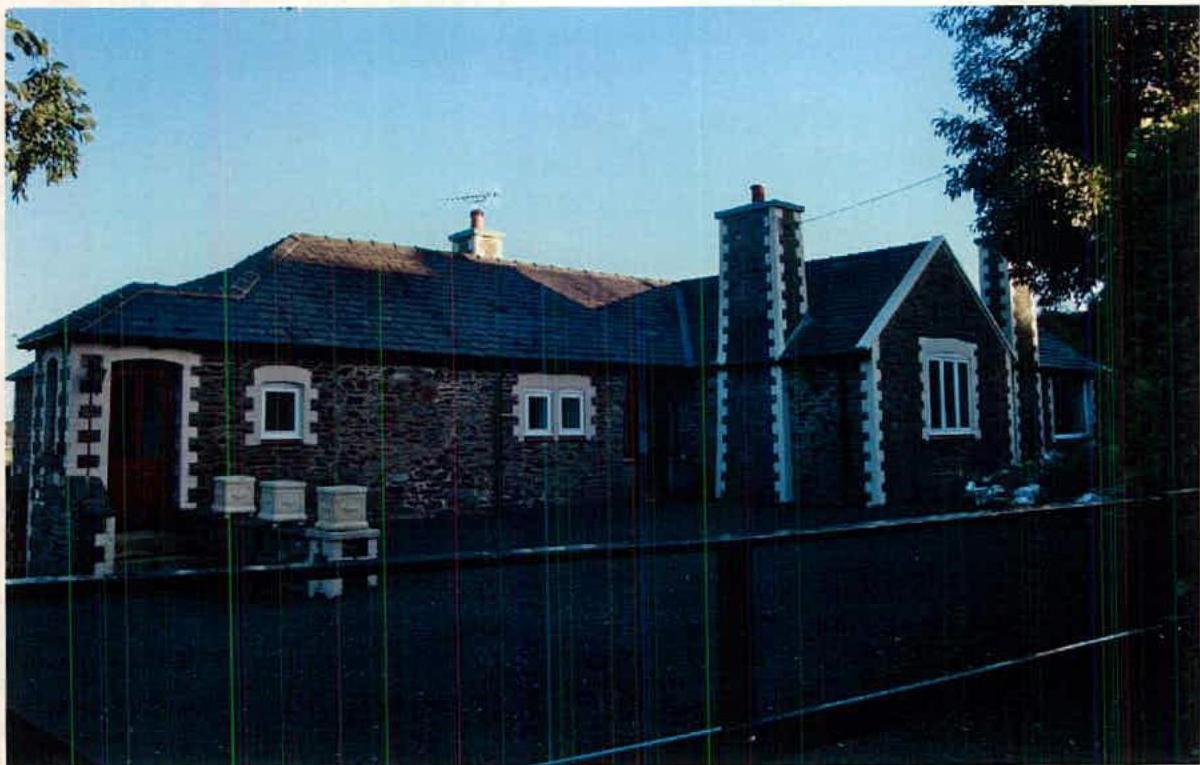 A grainy photograph of a single-story stone detached house featuring white quoins and a slate roof.