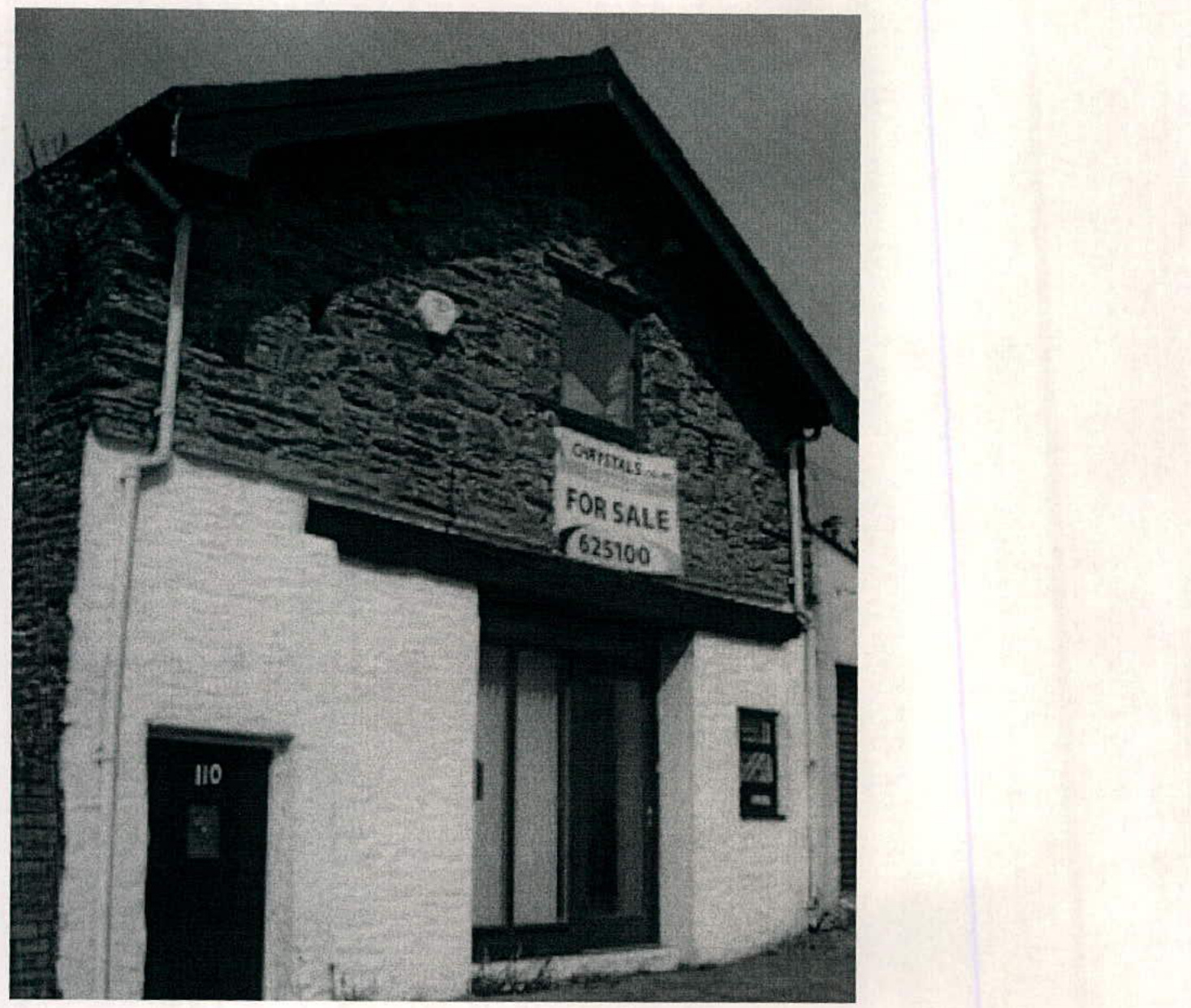 A black and white photograph of a two-story building with a stone upper facade and white lower facade, featuring a 'For Sale' sign.