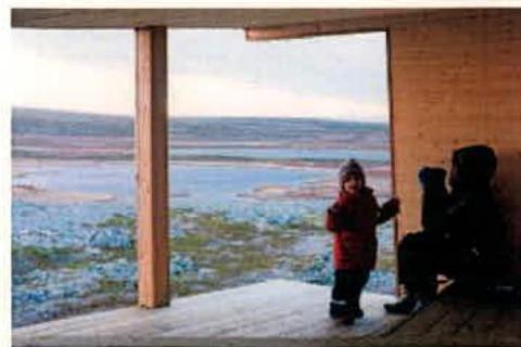 A photograph showing a wooden viewing platform or deck with people standing on it, overlooking a coastal marshland landscape.
