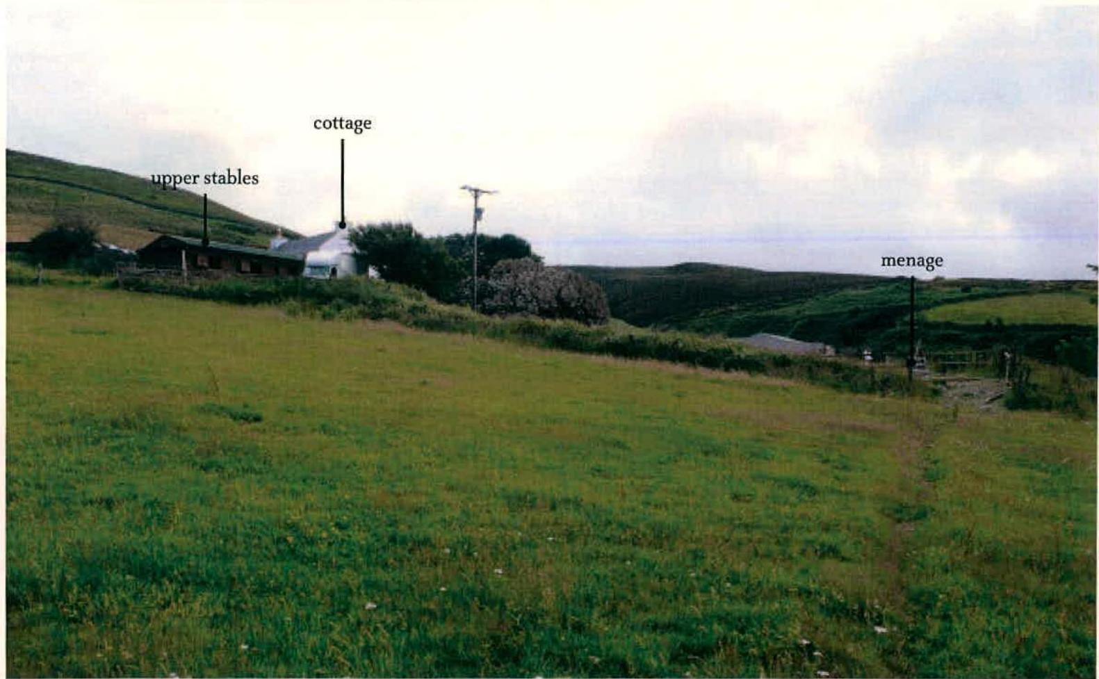 A photograph of a rural hillside showing existing structures labeled as 'upper stables', 'cottage', and 'menage'.