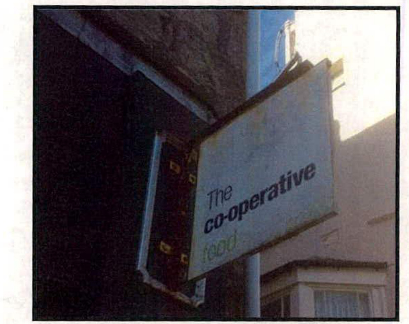 A photograph showing a hanging sign for 'The co-operative food' attached to the exterior wall of a building.