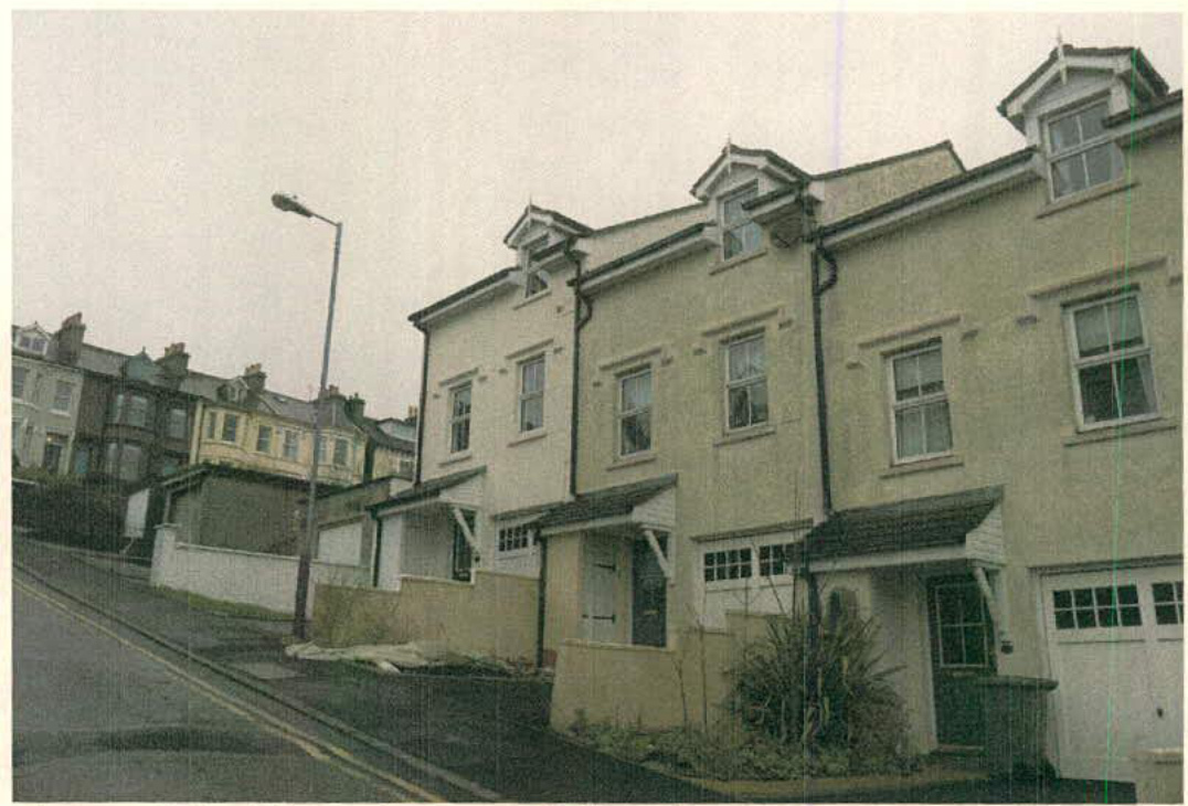 A street-level photograph showing a row of terraced houses featuring integrated garages and dormer windows.