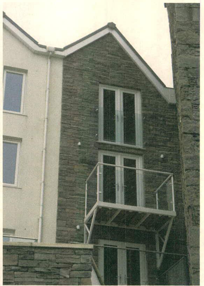 A photograph showing the exterior elevation of a modern residential building featuring stone cladding, white rendering, and a metal balcony.