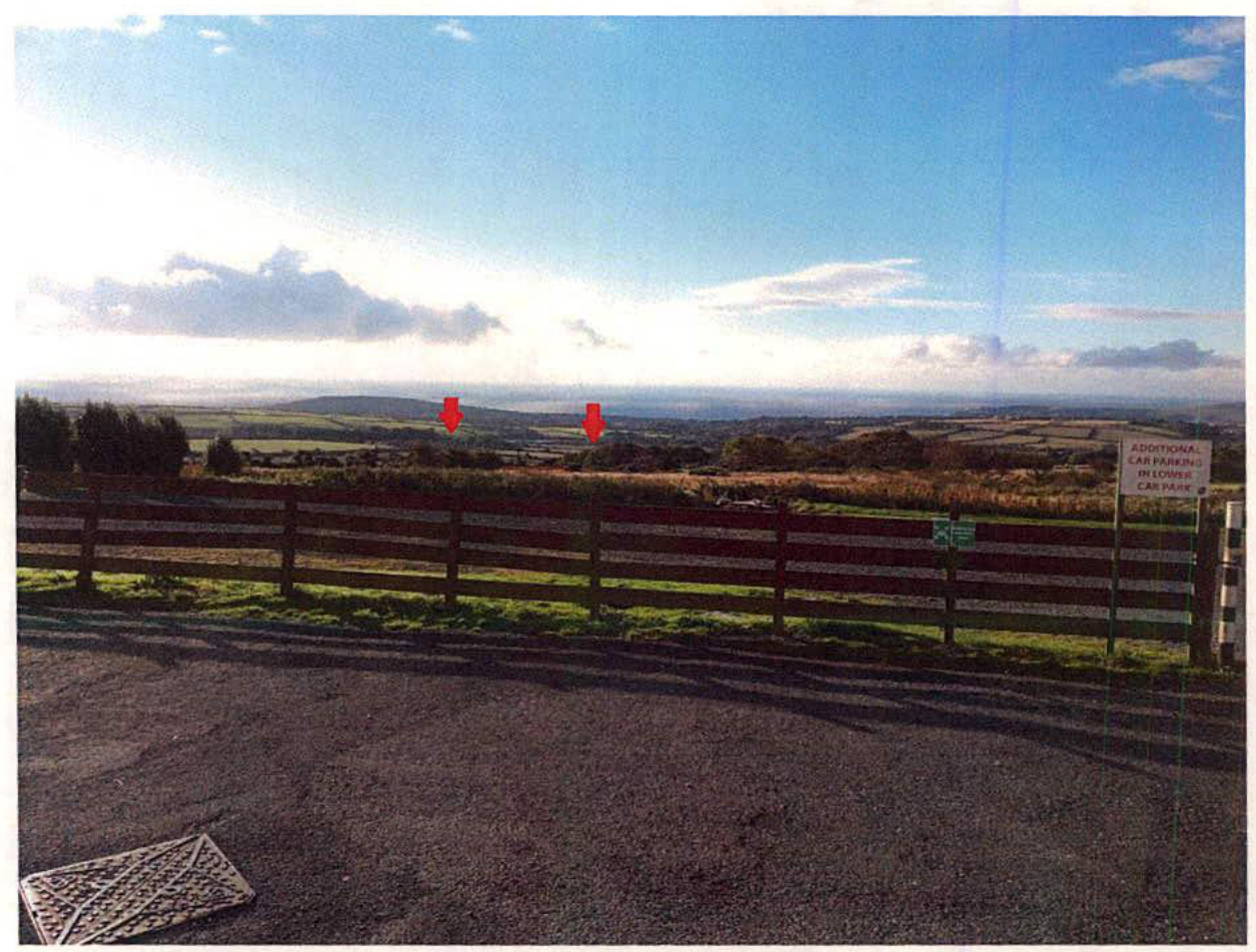 A photograph looking out from a car park over a rural landscape towards the coast, with red arrows indicating proposed building plot locations in the distance.