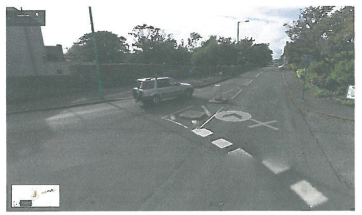 A street-level photograph showing road markings and a vehicle, likely depicting the site access, with a small location map inset in the bottom left corner.