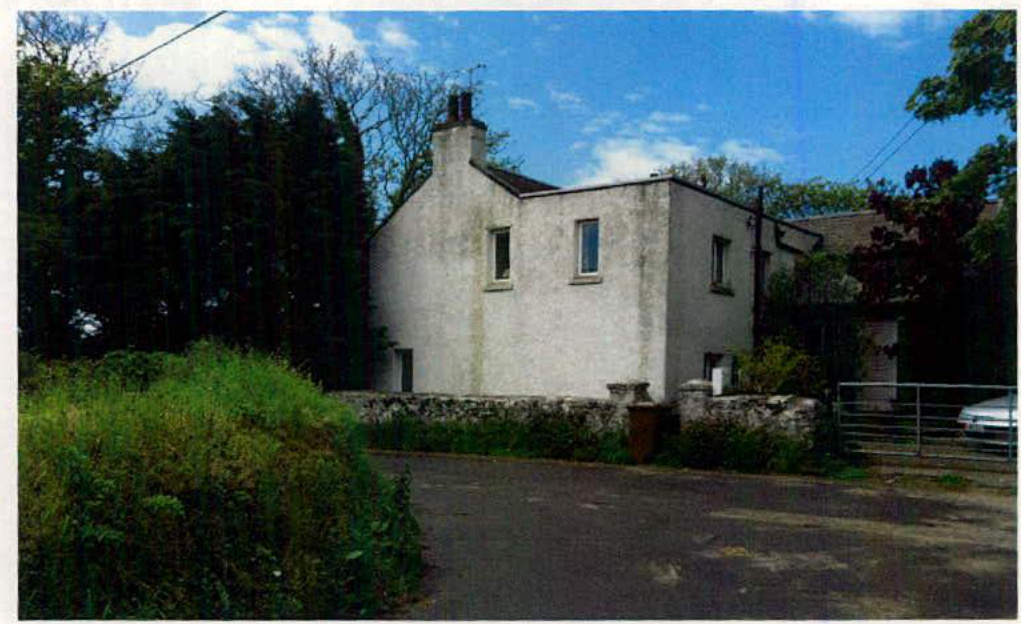 A photograph showing a white, two-story building, likely the redundant barn mentioned in the application, situated in a rural setting with a stone wall and driveway.