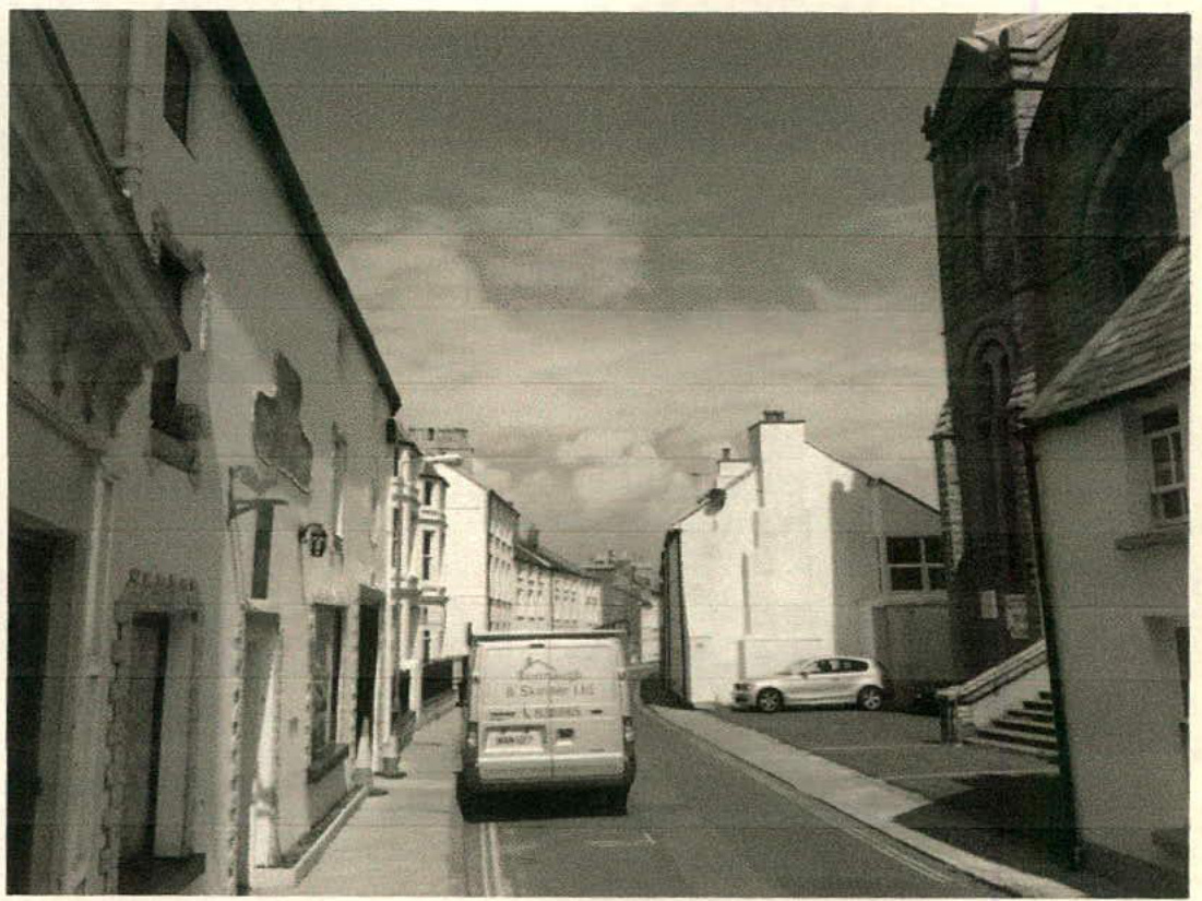 A black and white photograph showing a street scene with a row of terraced buildings on the left and a large stone church on the right.