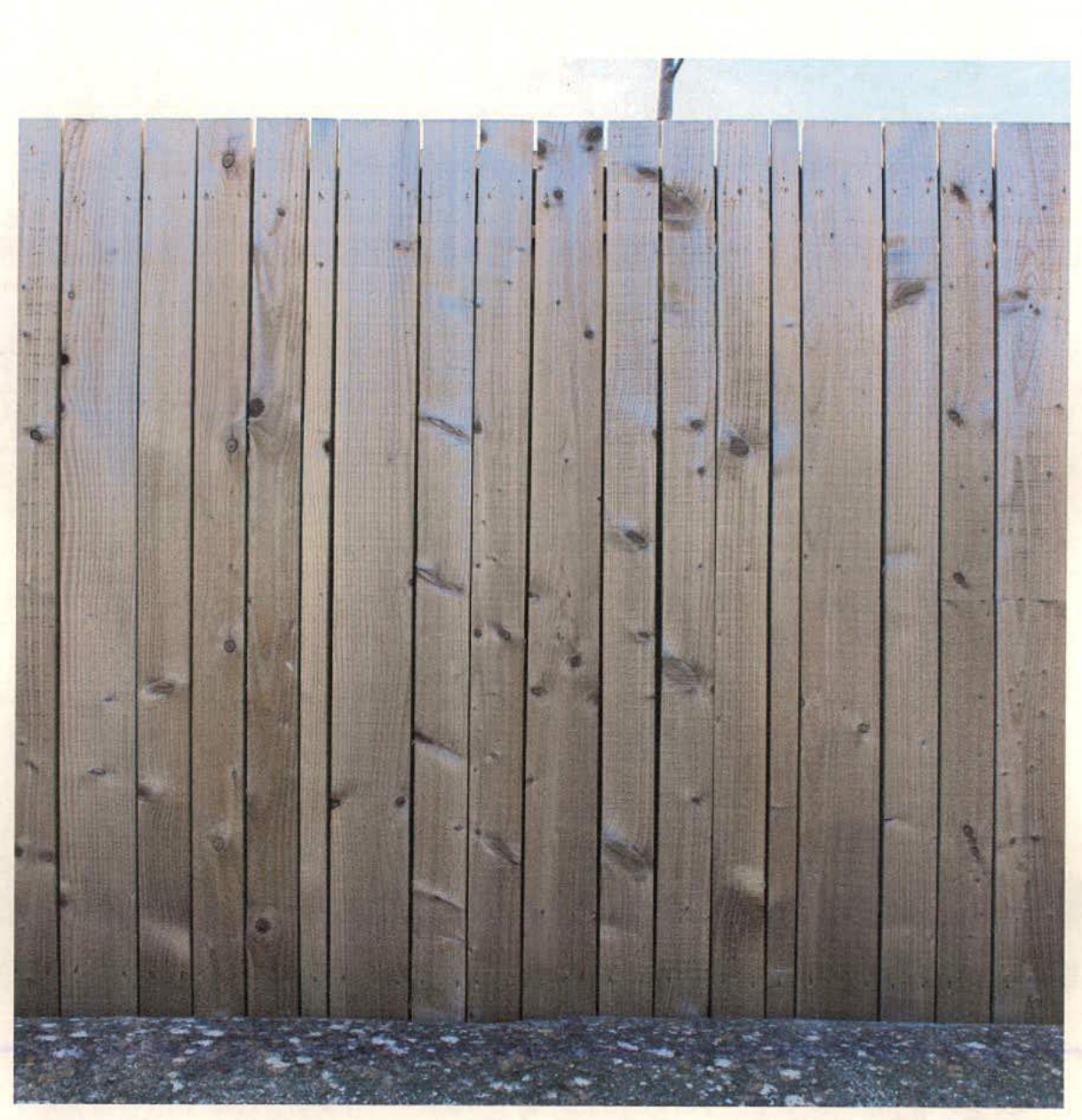 A close-up photograph showing a section of vertical wooden plank fencing with a concrete base.