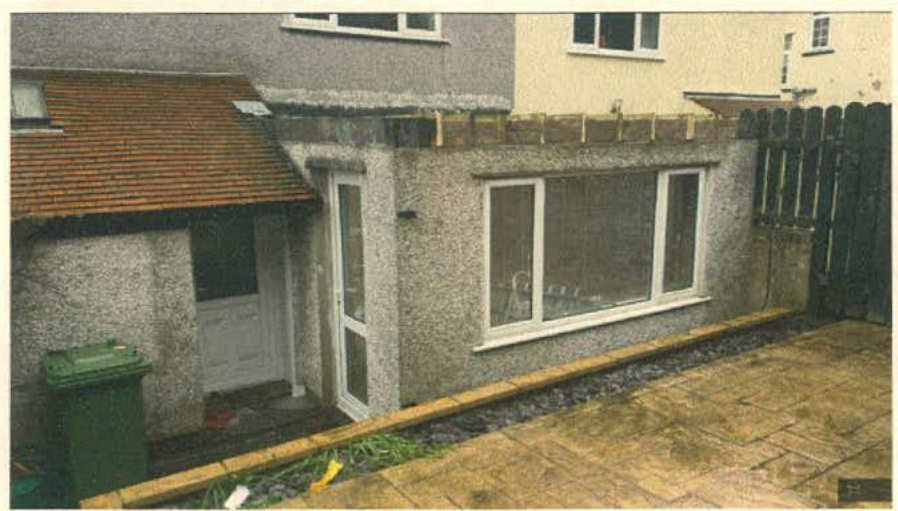 A photograph showing the rear exterior of a house featuring a single-storey extension with large windows and a flat roof section.