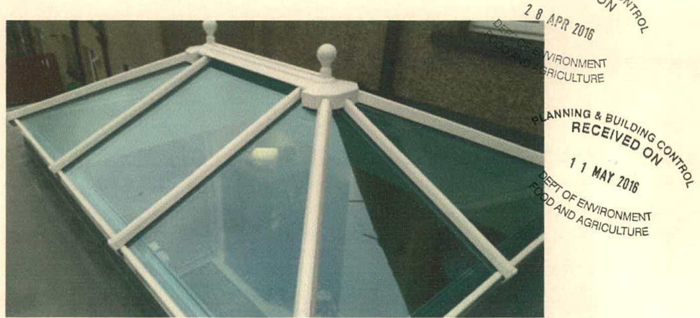 A close-up photograph of a white-framed glass roof lantern with a central finial and glazing bars, with planning stamps visible on the right.
