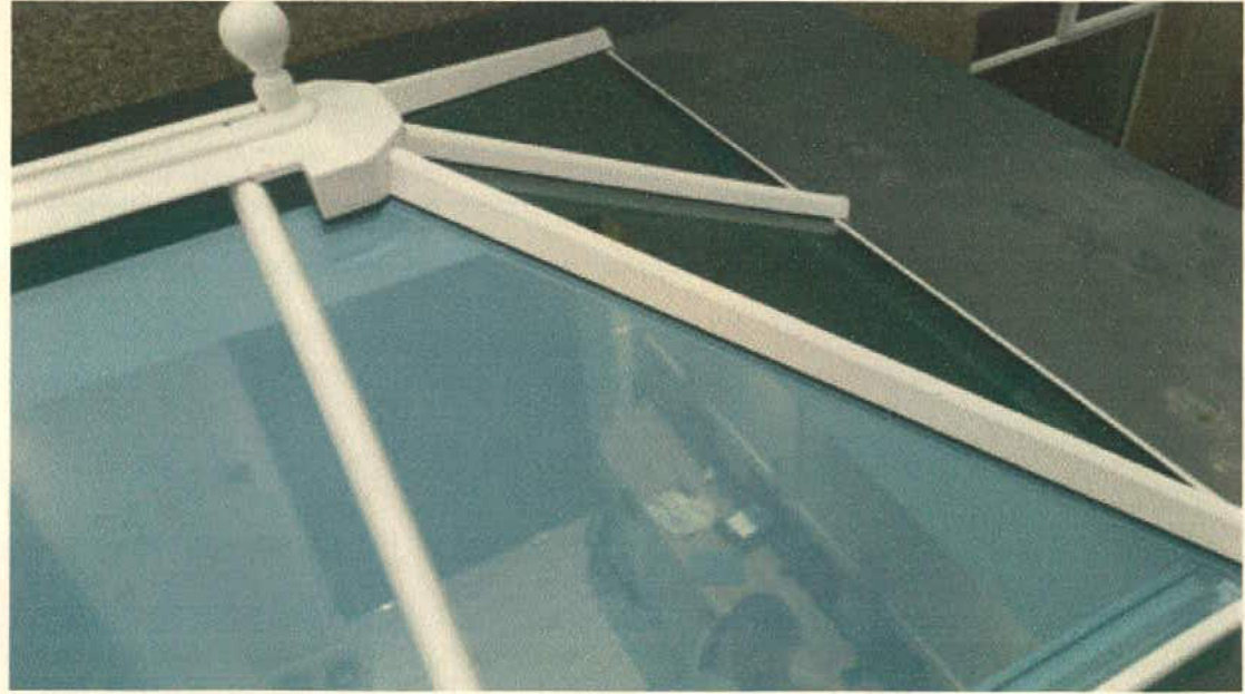 A close-up photograph showing a white-framed roof lantern installed on a roof, featuring glass panels and a central finial.