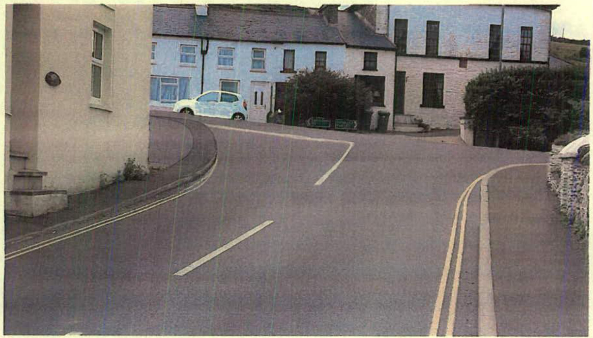 A street-level photograph showing a curved road leading up to a row of terraced houses with a white car parked nearby.