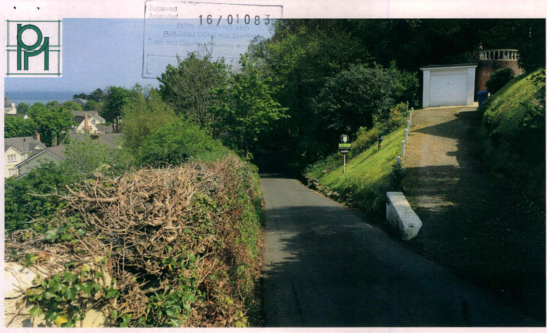 A photograph showing a road with a driveway leading up a grassy slope to a white garage, with coastal views visible in the distance.