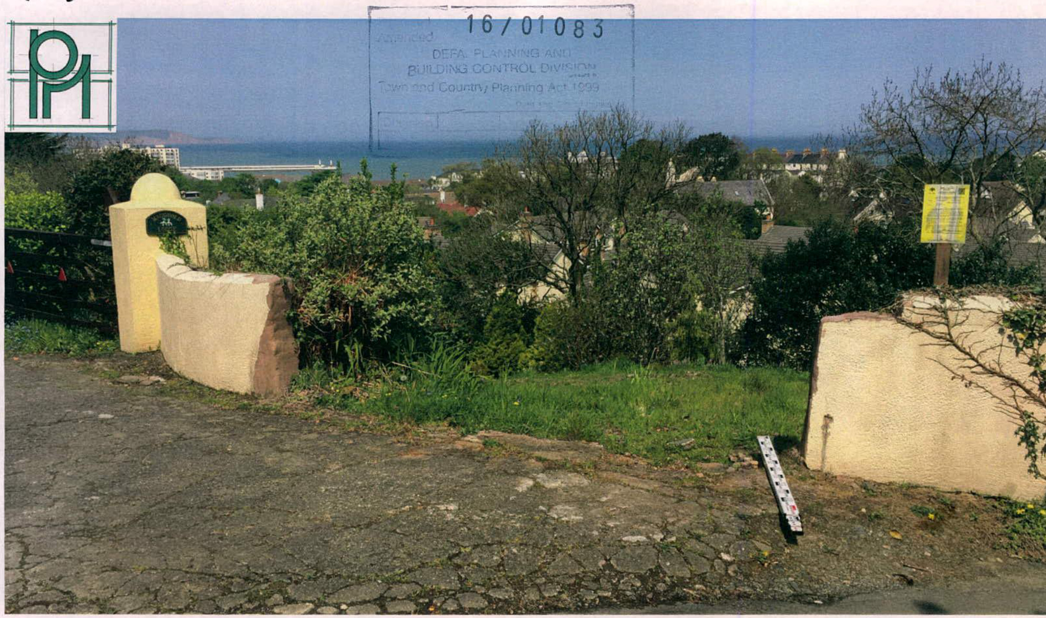 A photograph showing the site entrance with stone walls and a gatepost, overlooking a coastal view with houses and the sea in the distance.