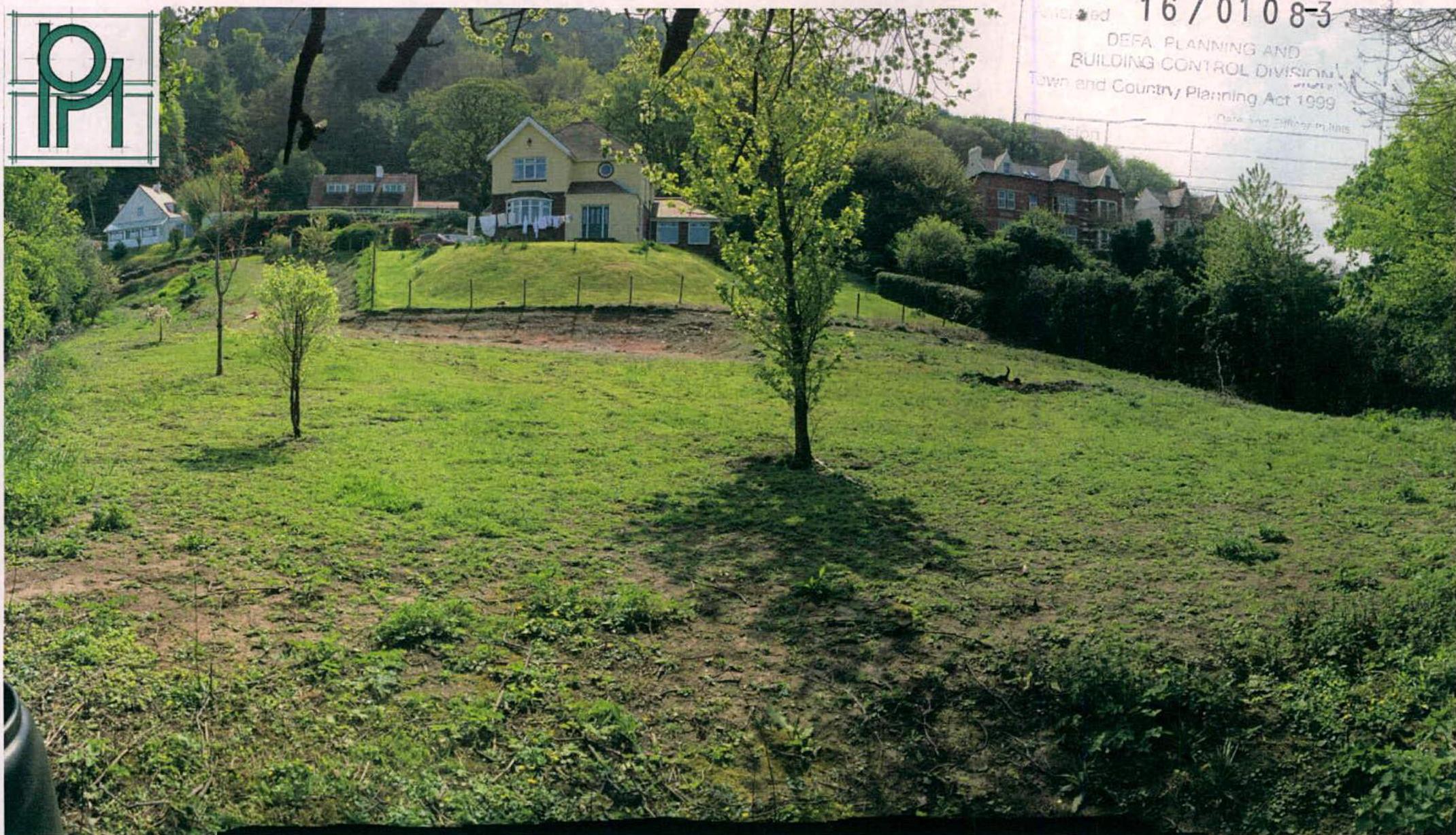 A photograph showing a grassy slope with young trees in the foreground and existing residential houses on a hill in the background.