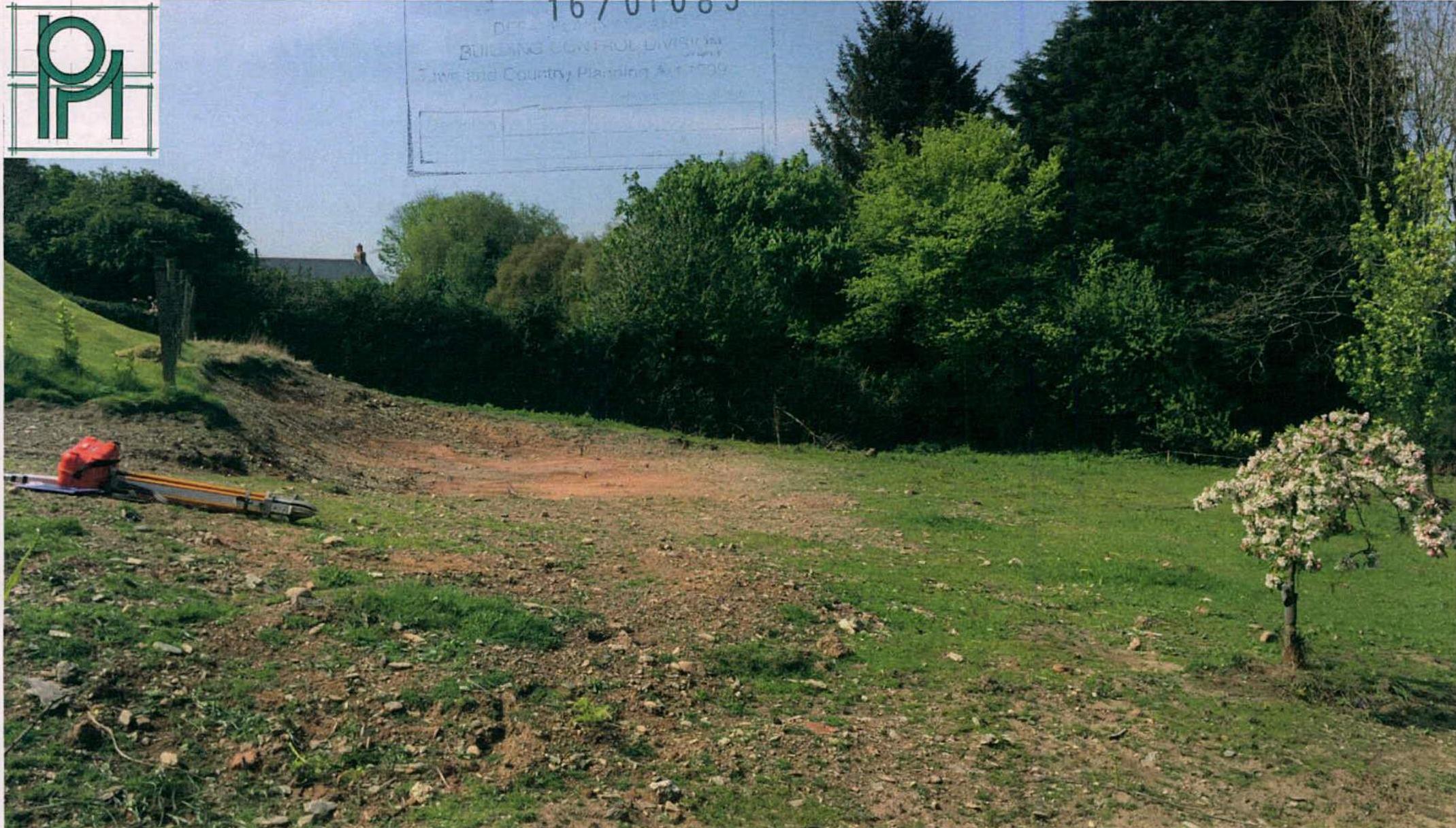 A photograph of a grassy rural plot of land with survey equipment in the foreground and trees in the background.