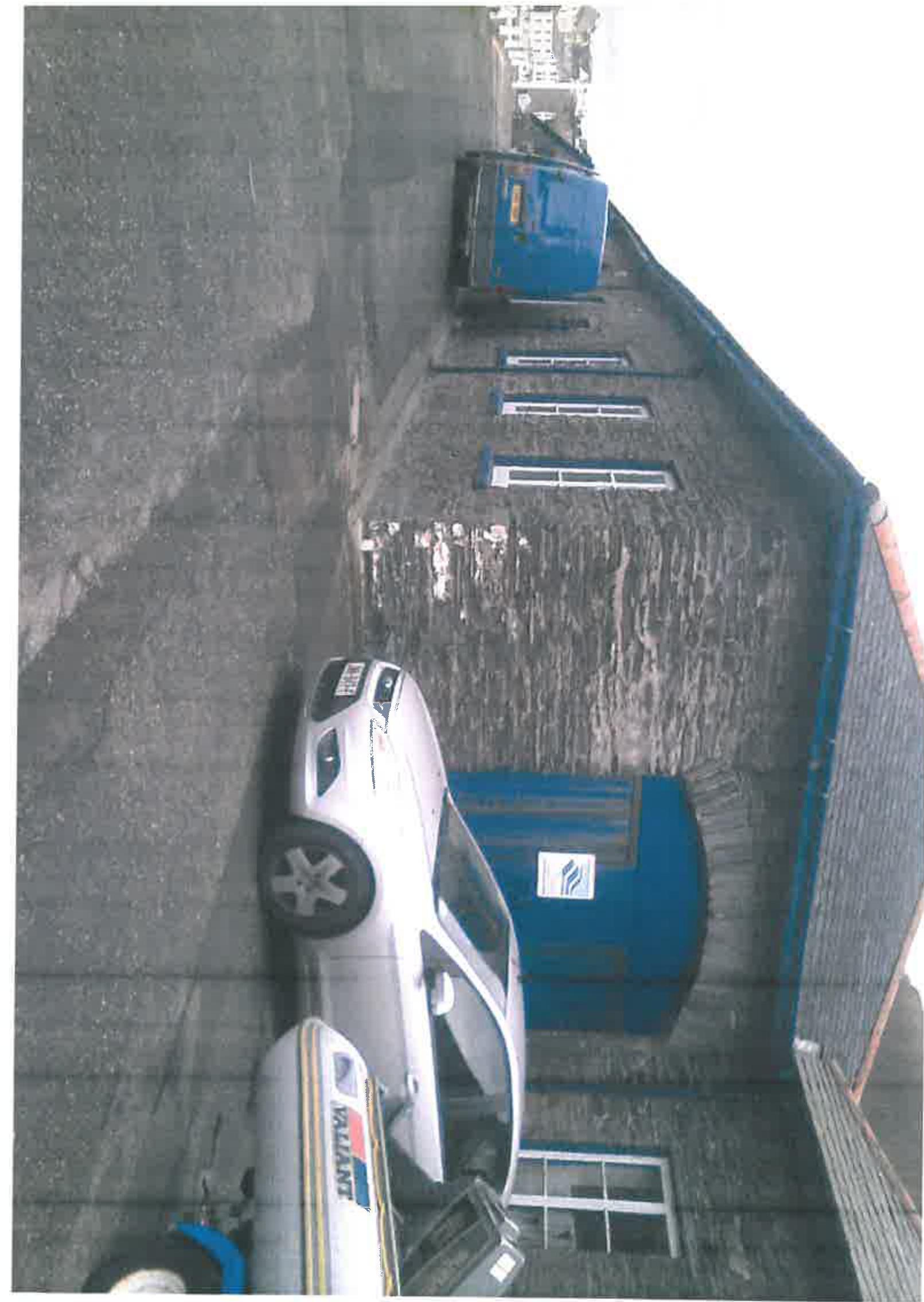A rotated photograph showing the side elevation of a stone building with a large blue roller shutter door and a white car parked in front.