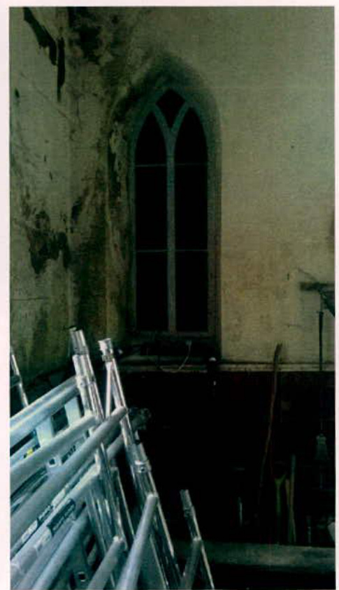 Interior photograph showing metal scaffolding and a large Gothic-style arched window within a building undergoing renovation.