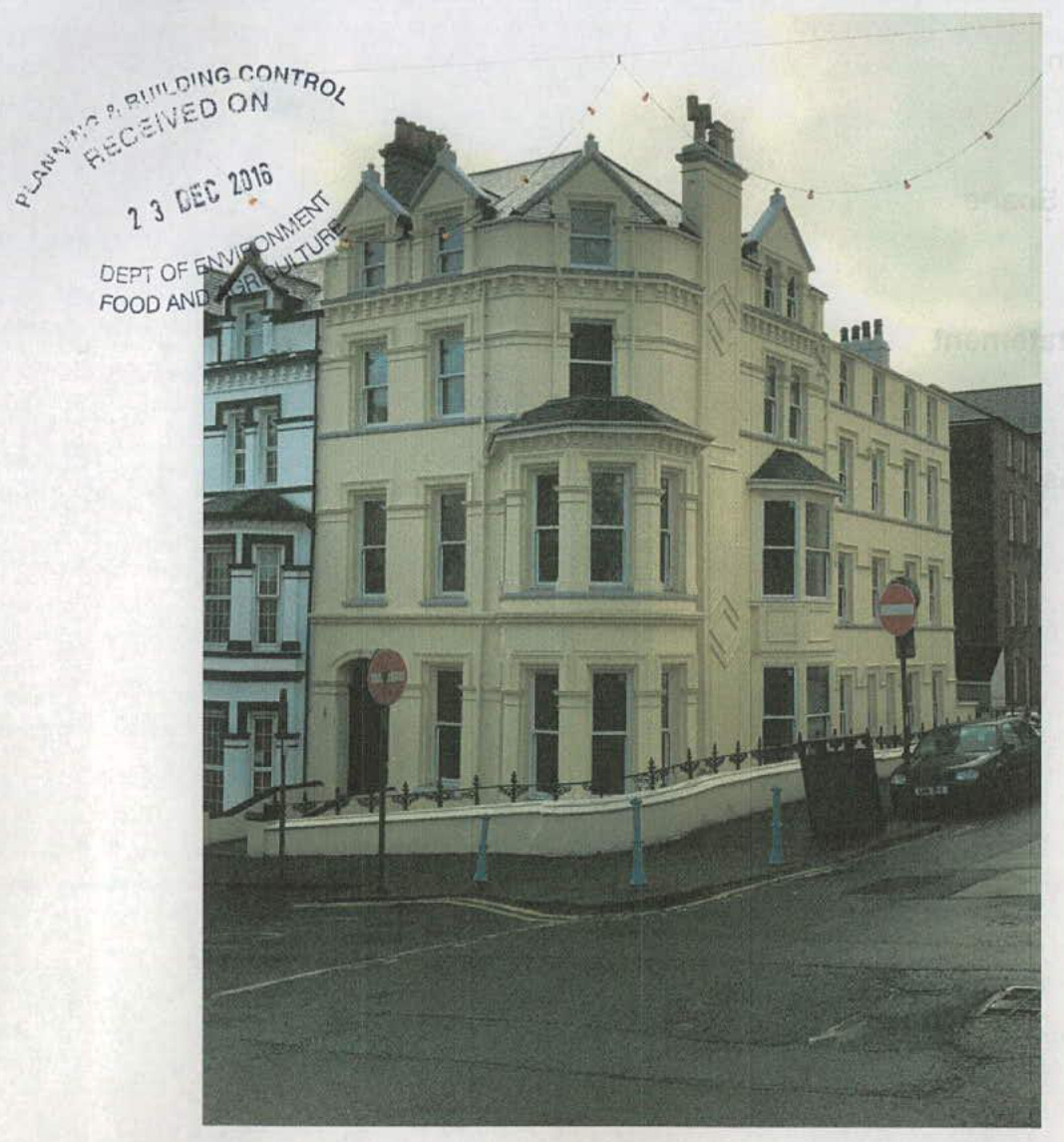 A street-level photograph of a large, cream-colored, multi-story terraced building on a corner, featuring bay windows and a low boundary wall.