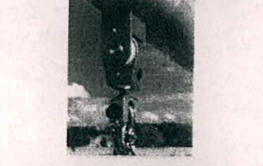 A very grainy, low-resolution black and white photograph depicting a piece of vertical play equipment, likely a swing set, with a person standing at the base.