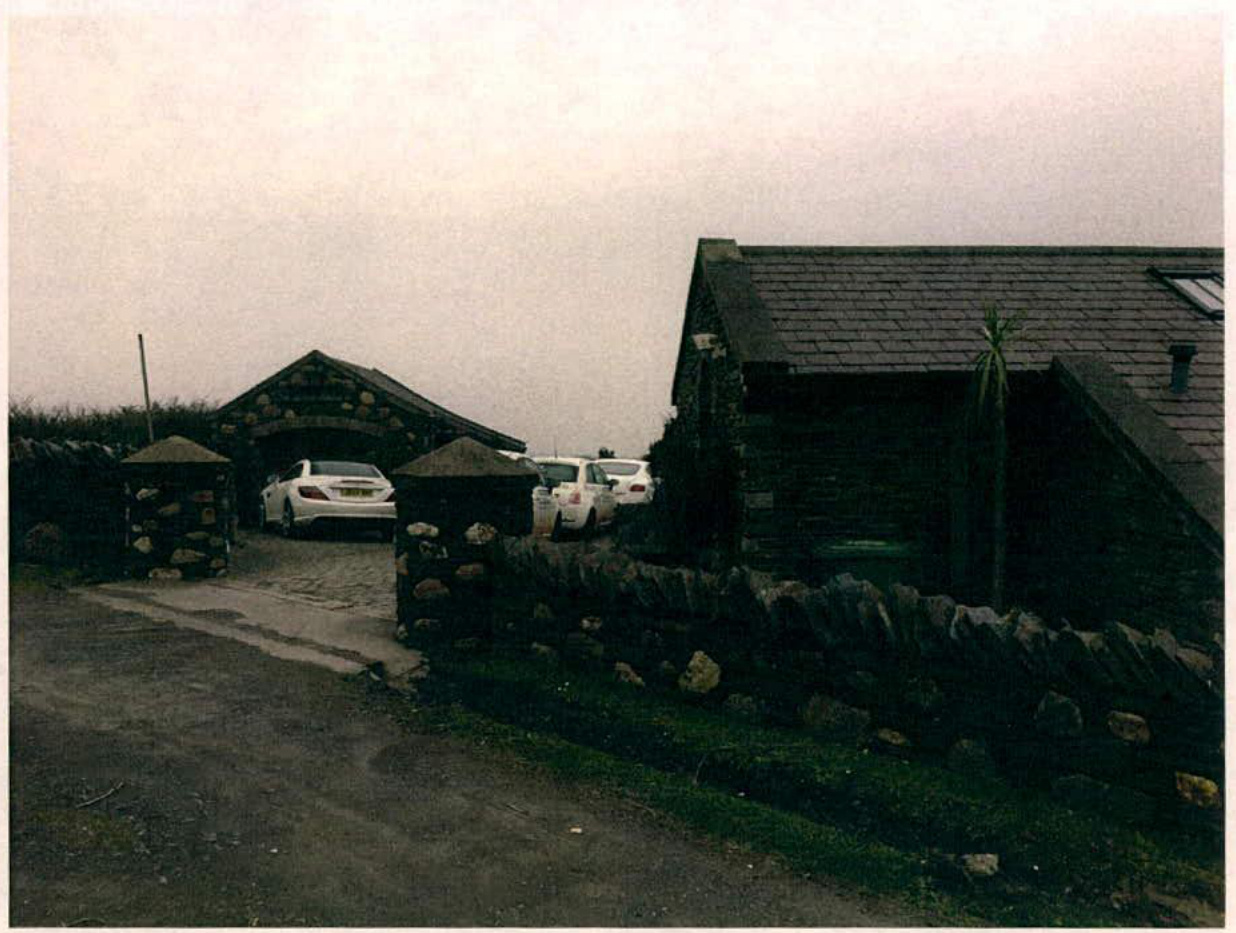 A photograph of a rural property featuring a stone house and a separate garage structure with cars parked in the driveway.