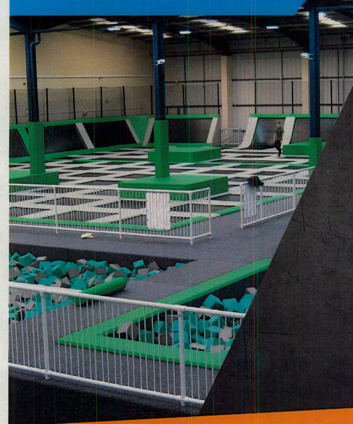 Interior photograph of a large leisure facility featuring trampolines, foam pits, and safety padding.
