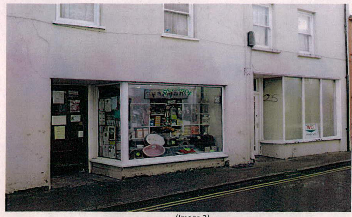 A street-level photograph showing the exterior of a white building with ground floor retail shop fronts and upper floor residential windows.
