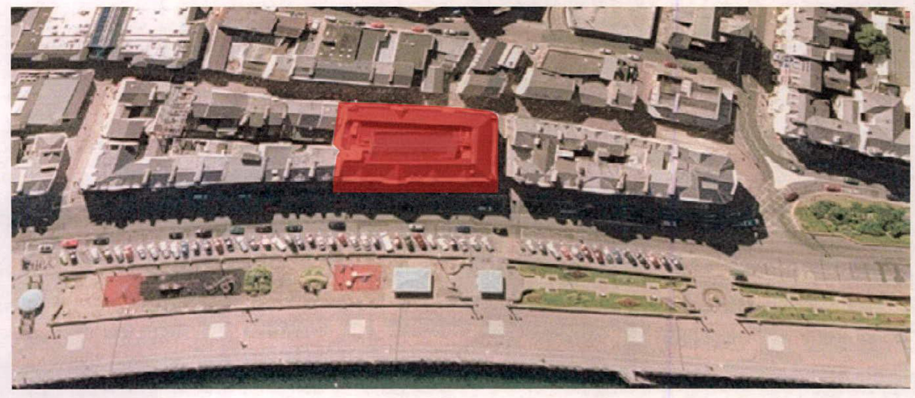 An aerial photograph showing a row of commercial buildings along a coastal promenade, with a specific building highlighted in red.
