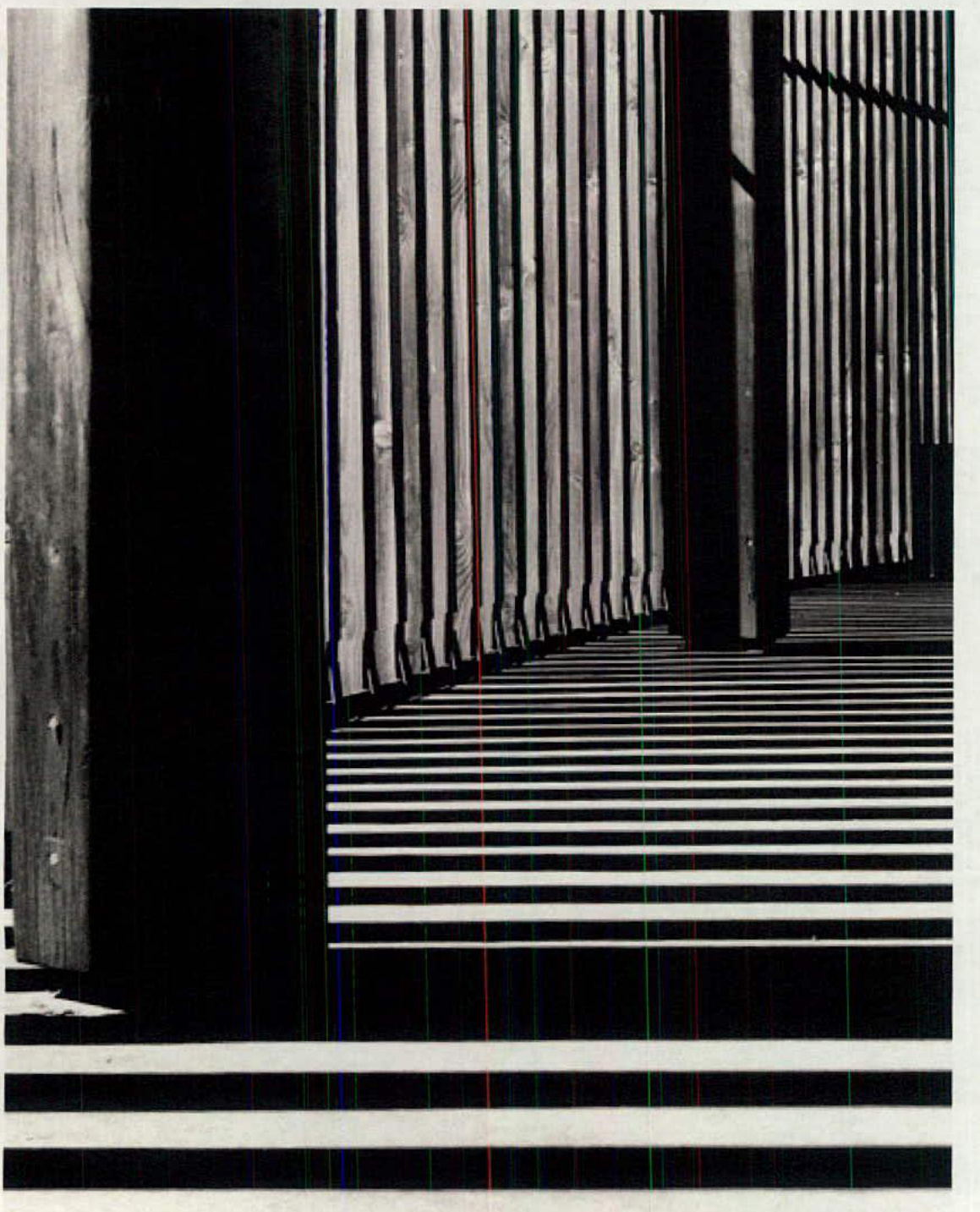 A close-up photograph showing vertical wooden slats or a screen casting strong horizontal shadows on a surface.