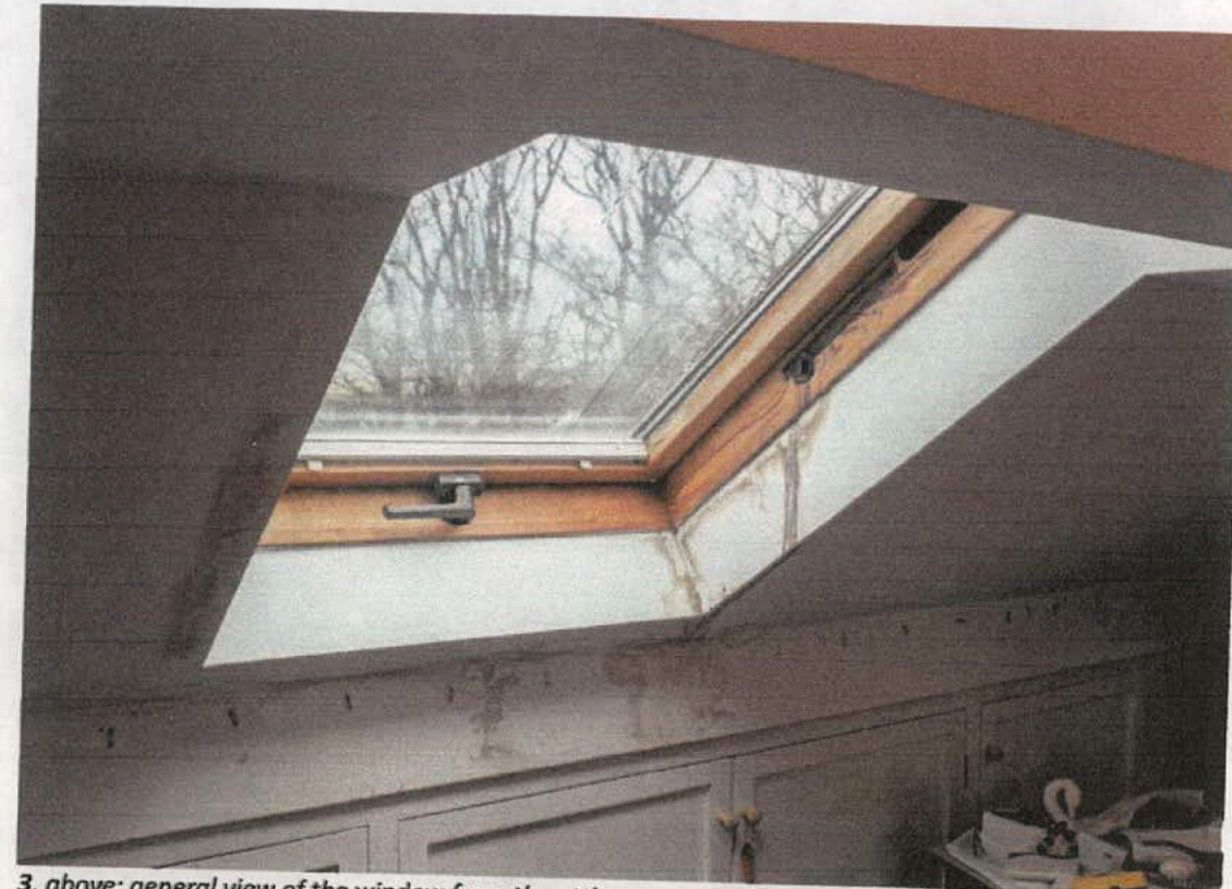 Interior photograph showing an open wooden skylight window set into a sloping roof with bare trees visible outside.