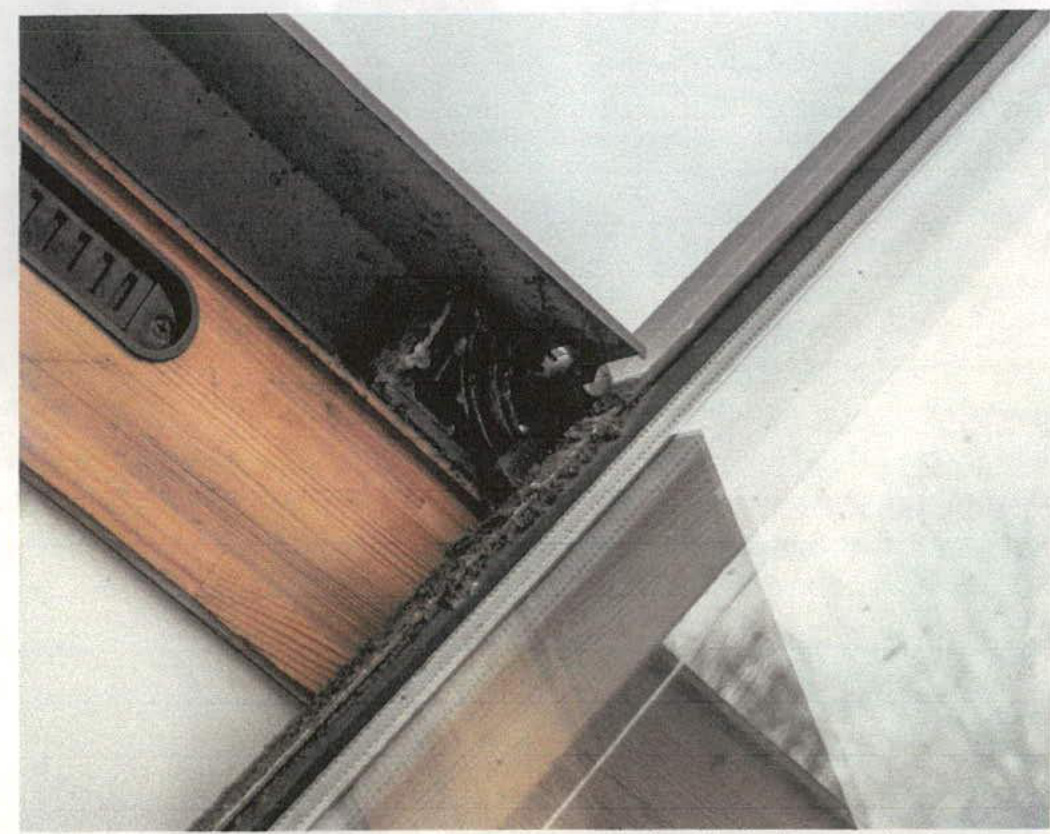 A close-up photograph showing the wooden and metal frame of a roof skylight, highlighting the junction with the roof structure and sealant.