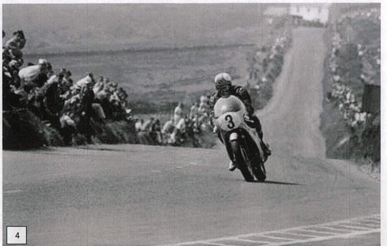 A black and white photograph showing a motorcycle racer on a road with spectators lining the embankment.