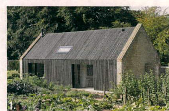 A photograph of a single-story building with a pitched roof and skylight, featuring vertical cladding on the front and stone walls on the side, surrounded by garden vegetation.