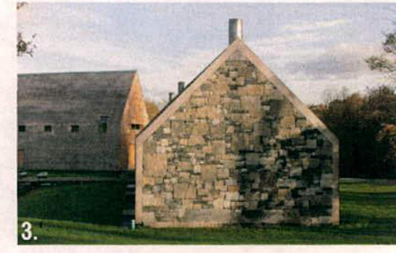 A photograph showing the gable end of a stone barn or outbuilding with a chimney, situated in a rural grassy area next to another similar structure.