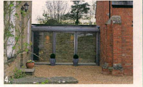 A photograph showing a single-story extension with large glass windows attached to an existing brick building, featuring a gravel patio area.