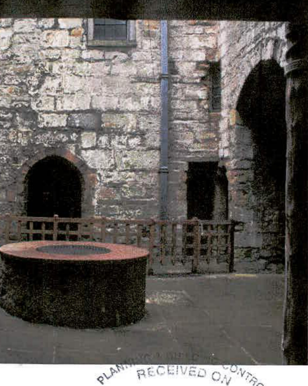 A photograph showing the stone interior courtyard of a historic keep, featuring arched openings, a wooden railing, and a circular stone structure.