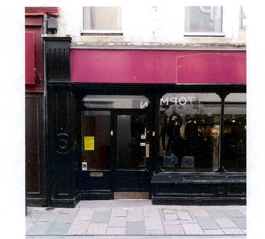A street-level photograph showing the existing facade of a commercial shop with a black painted frontage and large display windows, likely documenting the current state before proposed alterations.