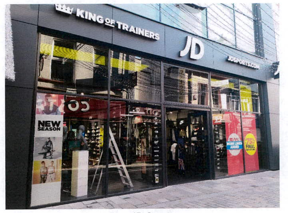 A street-level photograph of a commercial shop front featuring large glass curtain walling and 'JD' branding.