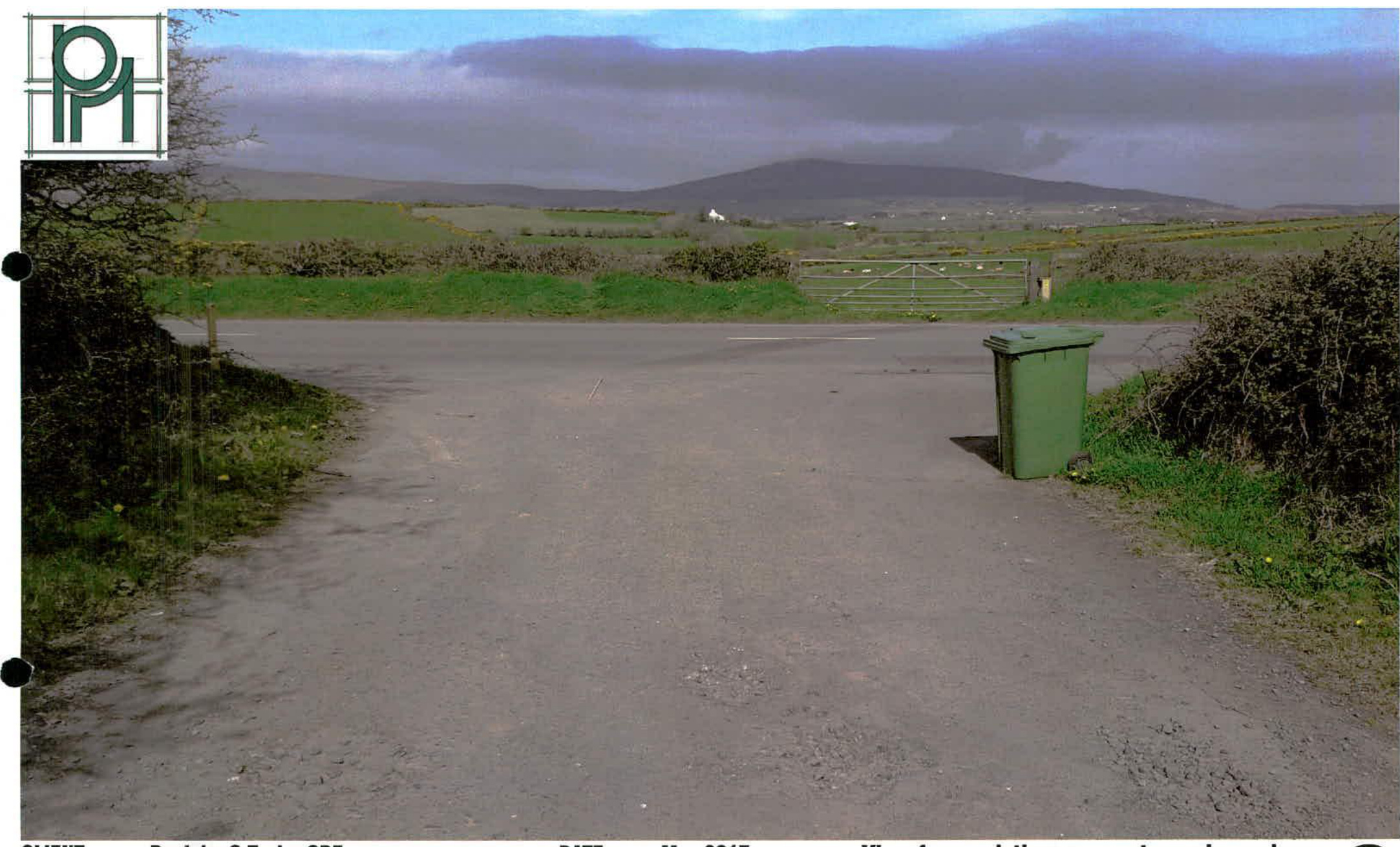 A photograph showing a rural paved access road with a green wheelie bin, hedgerows, and hills in the background.