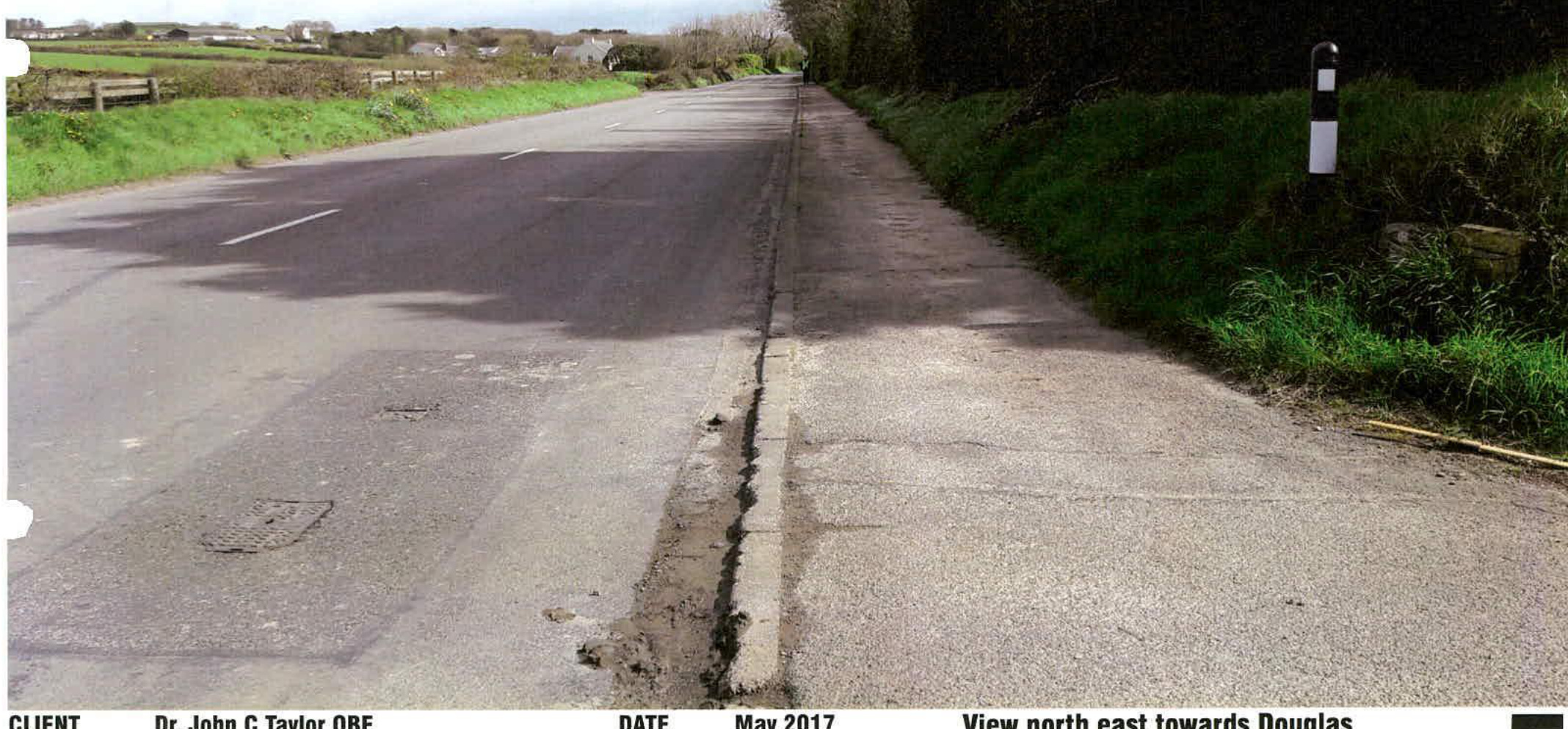 A photograph showing a paved rural road with grassy verges and a black and white bollard, looking north east towards Douglas.