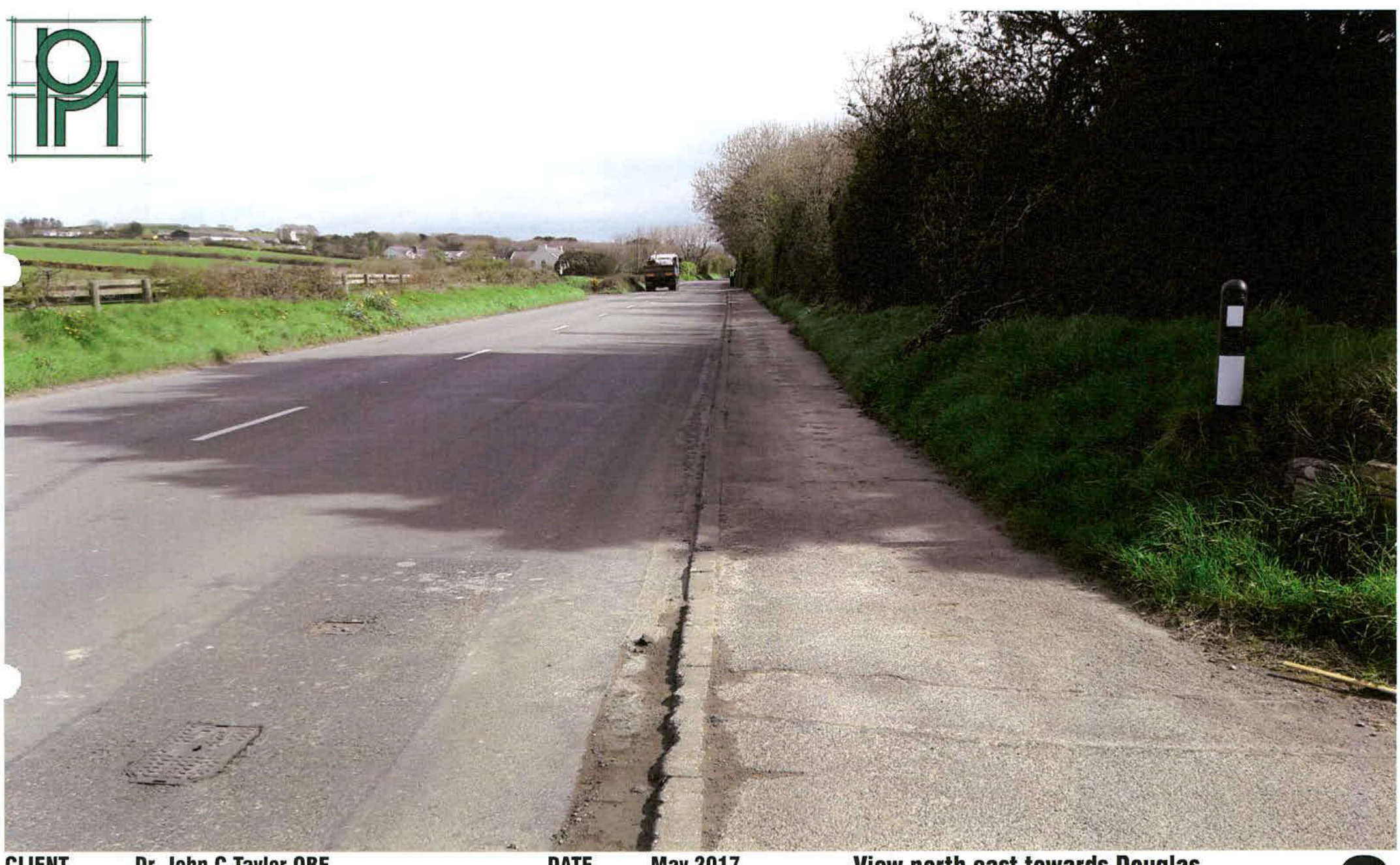 A photograph of a rural road with grassy verges and hedgerows, showing a vehicle in the distance. The caption identifies it as a view north east towards Douglas.