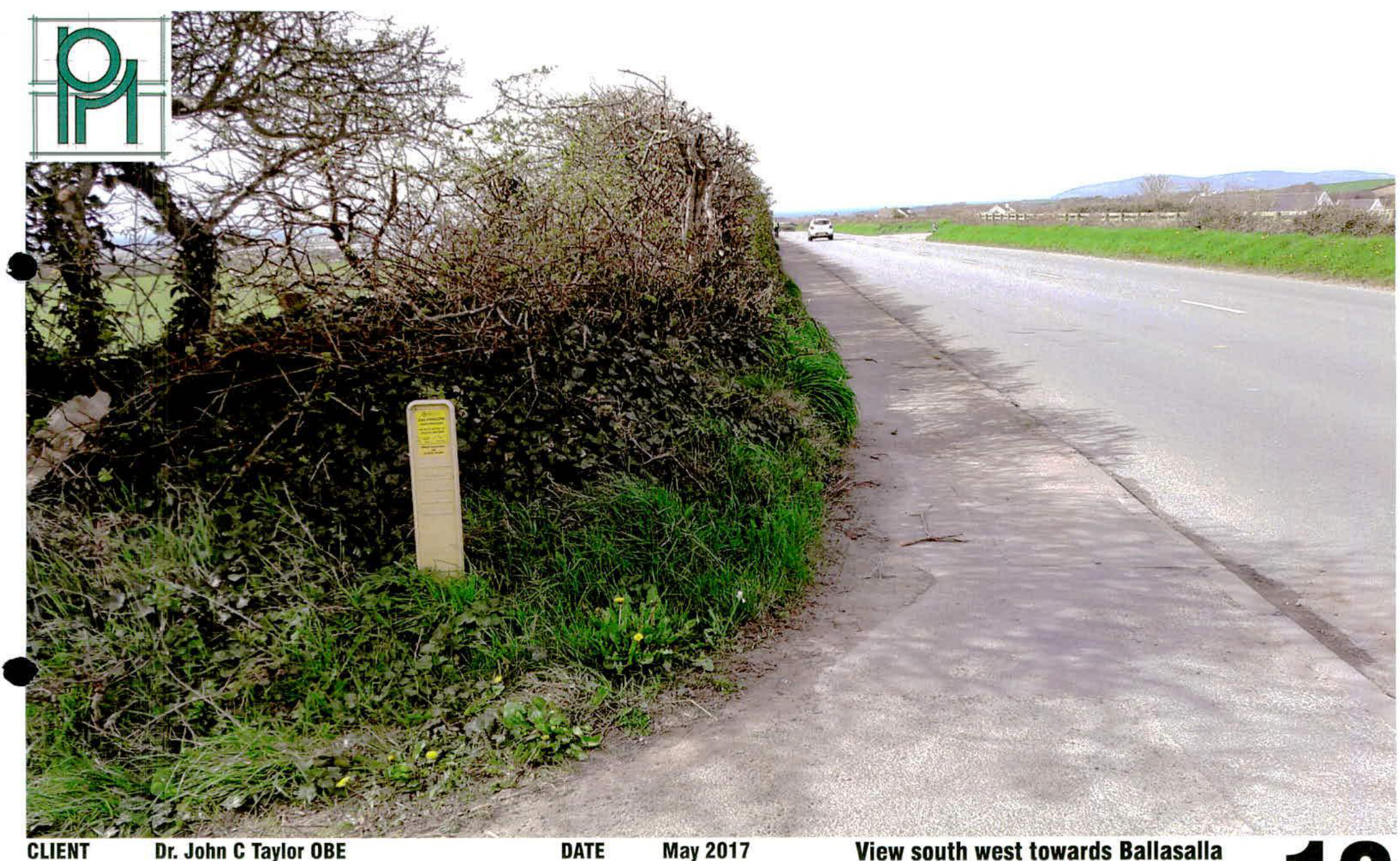 A photograph showing a rural road scene with a hedge on the left and a view towards Ballasalla in the distance, dated May 2017.