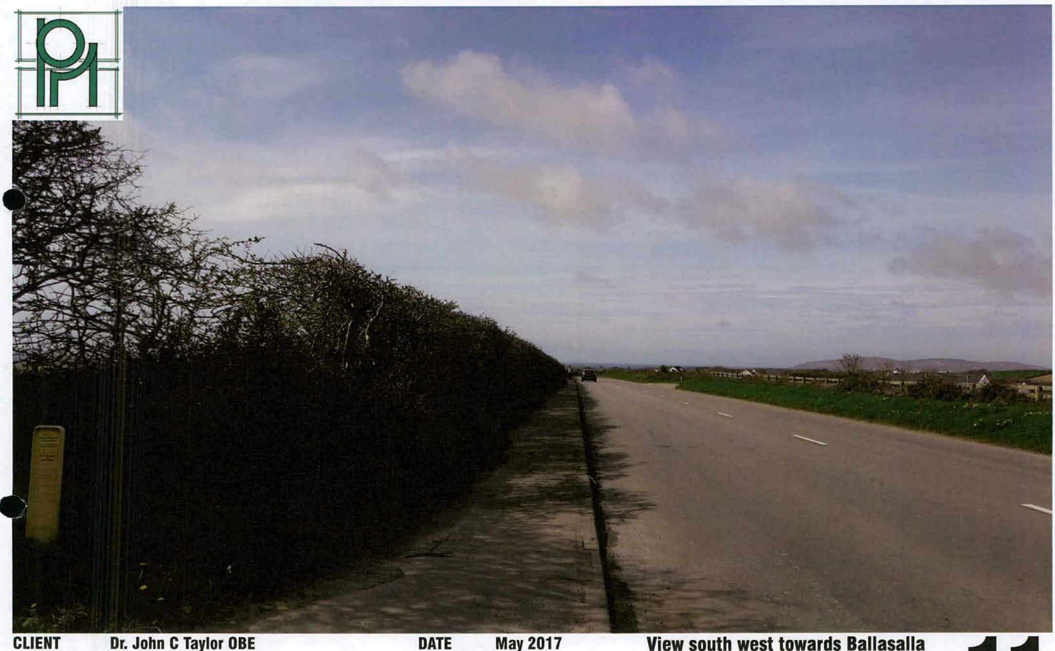 A photograph showing a rural road scene with a tall hedge on the left and fields on the right, captioned 'View south west towards Ballasalla'.