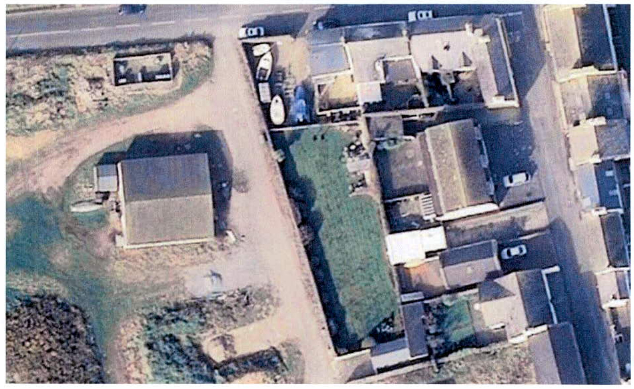 An aerial photograph displaying a detached building with a driveway on the left and a row of terraced residential houses on the right.