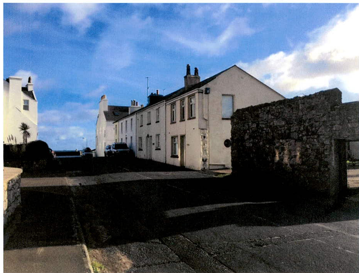 A street-level photograph showing a row of white terraced houses and a stone wall in the foreground.