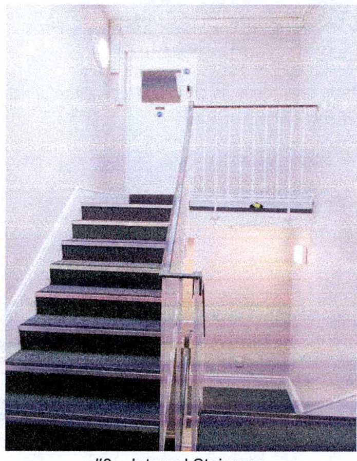 A grainy photograph showing an interior staircase with dark treads and a glass balustrade leading to a door on the upper landing.