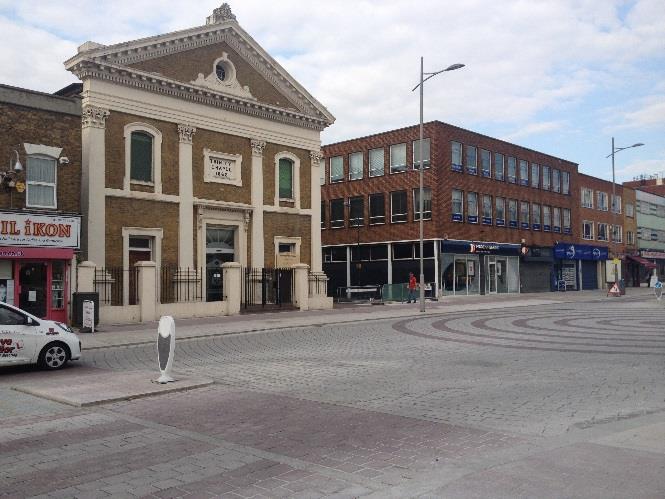 A street-level photograph showing the Trinity Chapel building and a paved promenade area in Douglas, Isle of Man, featuring circular stone patterns.