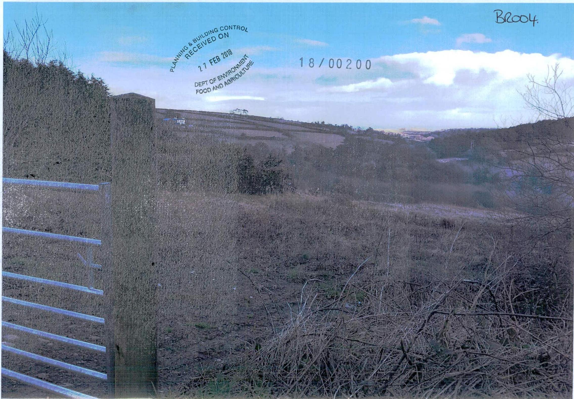 A photograph of a rural hillside site featuring a metal farm gate in the foreground and a stamp from the Planning & Building Control department.